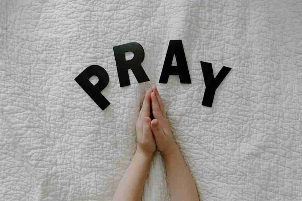 Praying Hands of a Person on White Textile